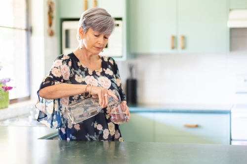 Middle aged woman pouring a glass of water in her kitchen - Australian Stock Image