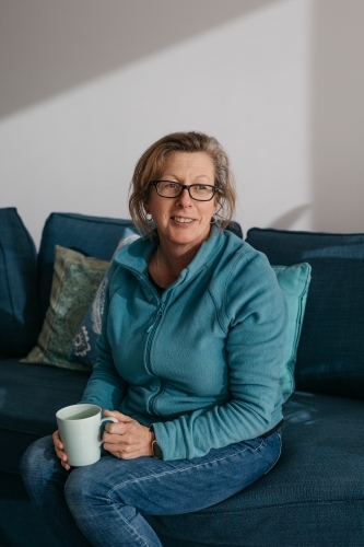 Middle aged woman sitting on couch, drinking hot beverage