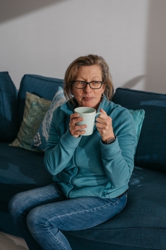 Middle aged woman sitting on couch, drinking hot beverage