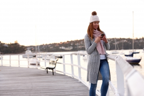 Middle aged woman using mobile phone on wharf wearing beanie - Australian Stock Image