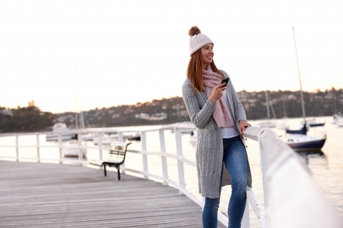 Middle aged woman using mobile phone on wharf wearing beanie - Australian Stock Image