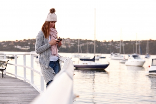 Middle aged woman using mobile phone on wharf wearing beanie - Australian Stock Image