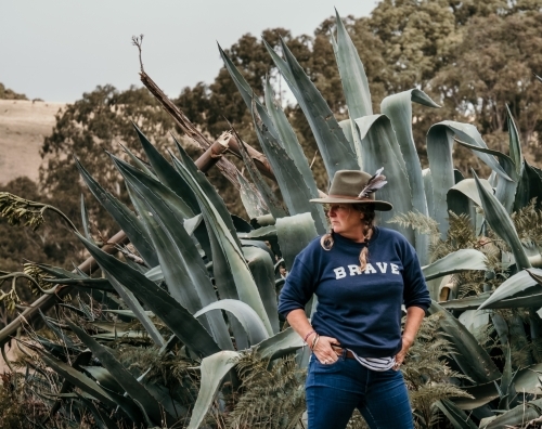 MIddle aged woman wearing a hat in front of a big Cactus plant outdoors. - Australian Stock Image