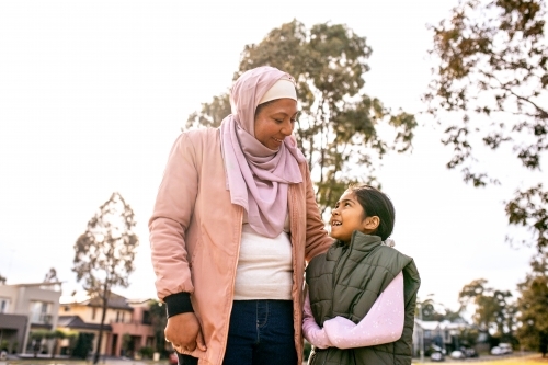 Middle aged woman wearing pink hijab and a girl wearing green coat looking at each other - Australian Stock Image