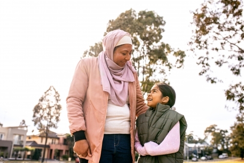 Middle aged woman wearing pink hijab and a girl wearing green coat looking at each other