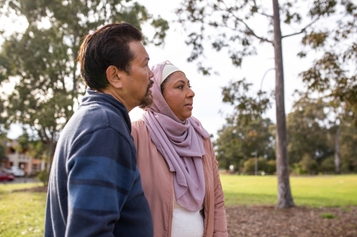 middle aged woman wearing pink hijab and middle aged man wearing blue sweater looking away