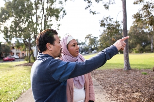 middle aged woman wearing pink hijab and middle aged man wearing blue sweater pointing