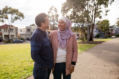 middle aged woman wearing pink hijab and smiling middle aged man looking at each other on a big lawn
