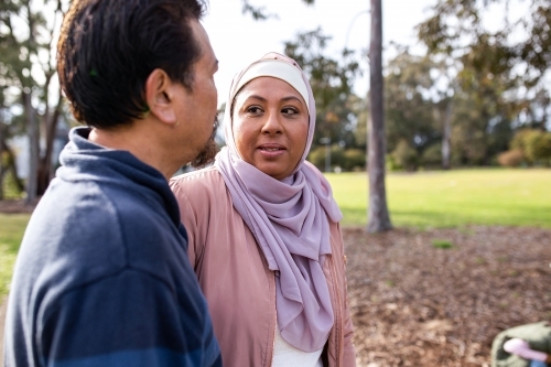 Middle aged woman wearing pink hijab looking at a middle aged man wearing blue sweater on a big lawn