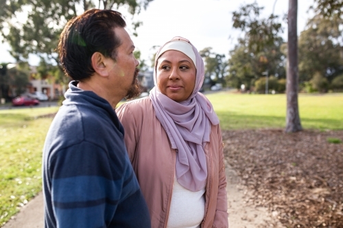 Middle aged woman wearing pink hijab looking at a middle aged man wearing blue sweater on a big lawn