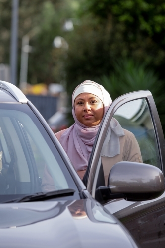 Middle aged woman wearing pink hijab opening the driver seat car door