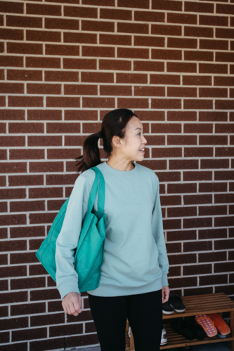 Middle-aged woman with a teal tote bag standing in front of a brick wall. - Australian Stock Image