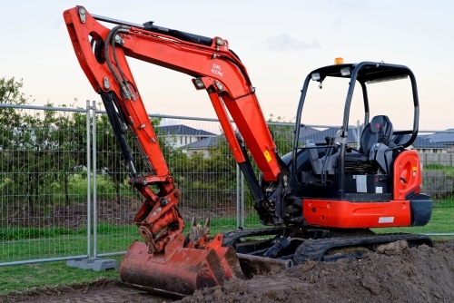 Mini digger standing idle at a construction site - red excavator - Australian Stock Image