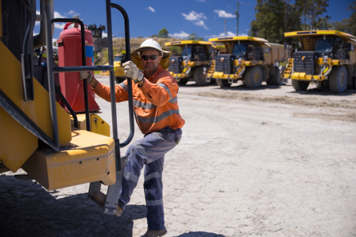 Mining operator man holding on the handrails while climbing up the dump truck - Australian Stock Image