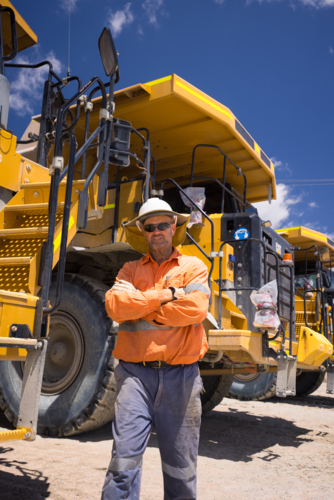Mining operator man with arms crossed standing next to a huge dump truck on mine site - Australian Stock Image