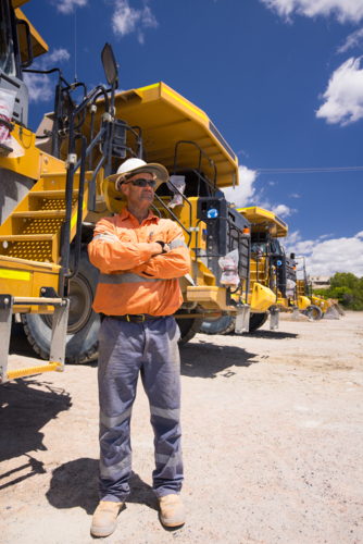 Mining operator man with arms crossed standing next to a huge dump truck on mine site - Australian Stock Image