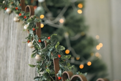 Mistletoe and delicate Christmas lights strewn along rustic wooden seat. Golden bokeh in background. - Australian Stock Image