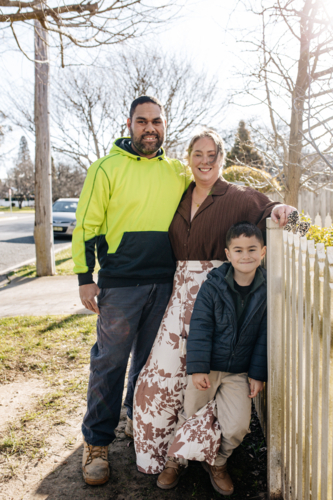 Mixed ethnicity couple with their younger son standing beside picket fence outdoors - Australian Stock Image