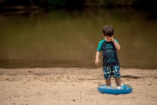 Mixed race 3 year old boy plays on a river bank with an inflatable swimming tube - Australian Stock Image