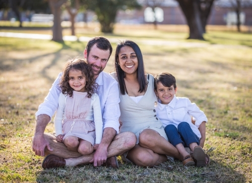Mixed race aboriginal and caucasian twins sitting with mum and dad on grass