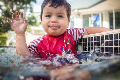 Mixed race baby boy swims and plays in a backyard pool