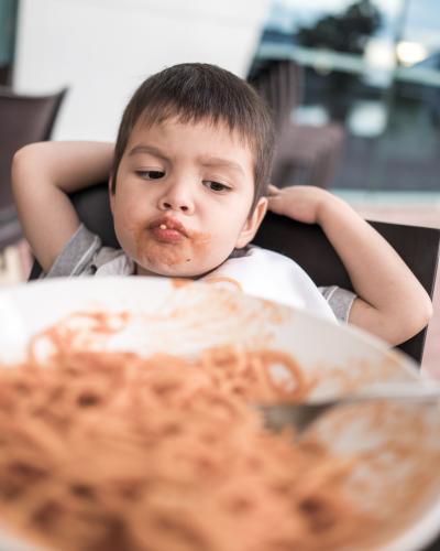 Mixed race boy eating pasta at a suburban Italian restaurant