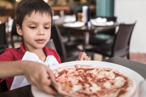 Mixed race boy eating pizza at a suburban Italian restaurant - Australian Stock Image