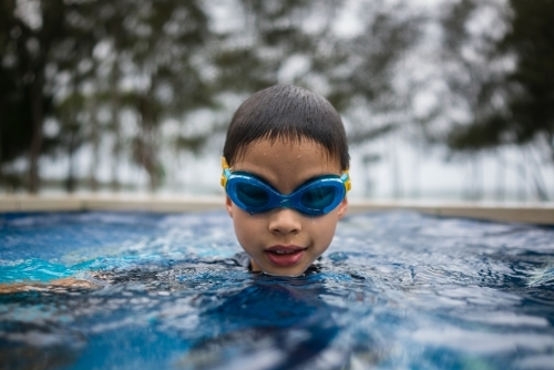 Mixed race boy playing in small backyard pool - Australian Stock Image