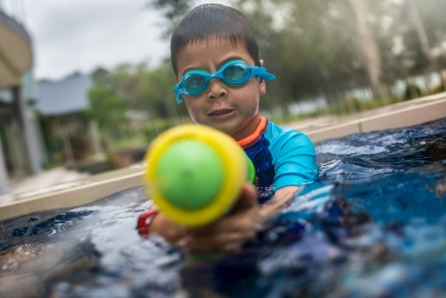 Mixed race boy playing in small backyard pool - Australian Stock Image