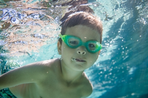 Mixed race boy swims and plays in a backyard pool - Australian Stock Image
