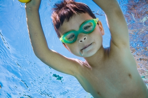 Mixed race boy swims and plays in a backyard pool - Australian Stock Image