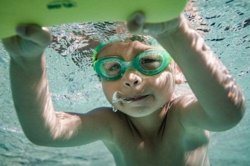 Mixed race boy swims and plays in a backyard pool - Australian Stock Image