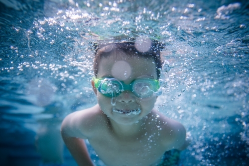 Mixed race boy swims and plays in a backyard pool - Australian Stock Image