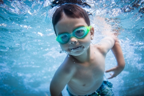 Mixed race boy swims and plays in a backyard pool - Australian Stock Image