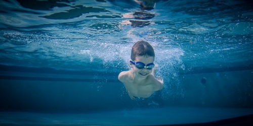 Mixed race boy swims and plays in a backyard pool - Australian Stock Image