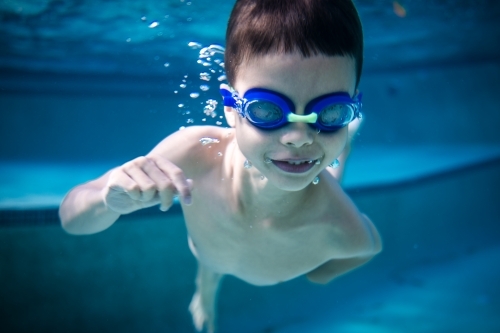Mixed race boy swims and plays in a backyard pool - Australian Stock Image