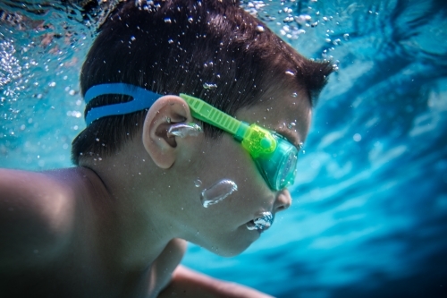 Mixed race boy swims and plays in a backyard pool - Australian Stock Image