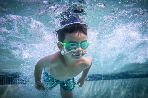 Mixed race boy swims and plays in a backyard pool - Australian Stock Image