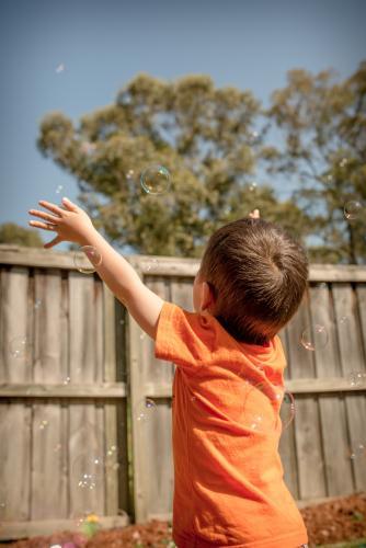 Mixed race boys play with bubbles in their suburban backyard - Australian Stock Image