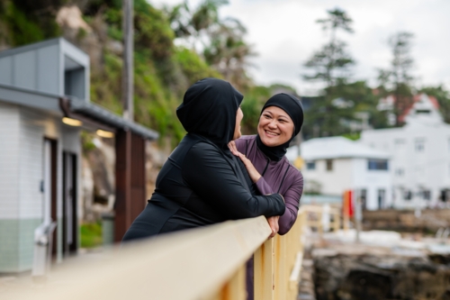 Mixed race women standing and leaning on the railings along coastal path while chatting - Australian Stock Image