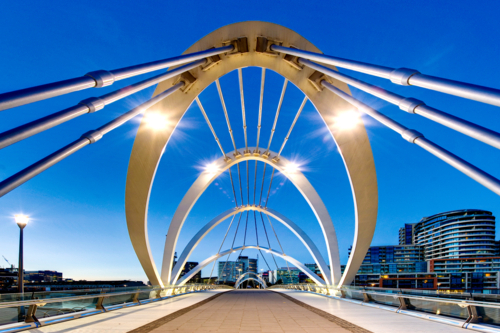 Modern pedestrian bridge framed by striking architectural arches at dusk - Australian Stock Image