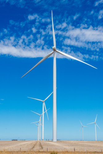 Modern wind turbines standing tall above dry farmland beneath a vivid blue sky - Australian Stock Image