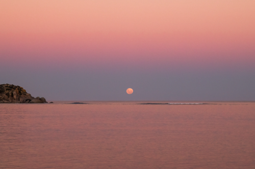 Moon going down over water with rocky island in foreground, Victor Harbor, South Australia - Australian Stock Image