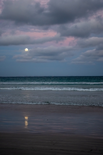 Moon reflected on the sand as it rises over the beach at sunset - Australian Stock Image