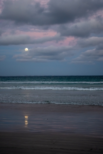 Moon reflected on the sand as it rises over the beach at sunset