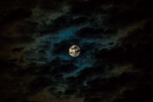 Moon with blue and white light covered with clouds - Australian Stock Image