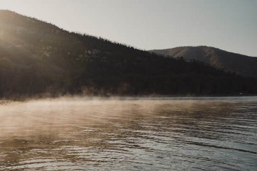 Morning fog lit up by the sun with mountains in the background - Australian Stock Image