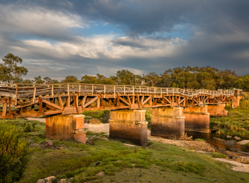 Morning sun on an old rickety railway bridge underneath a moody sky - Australian Stock Image