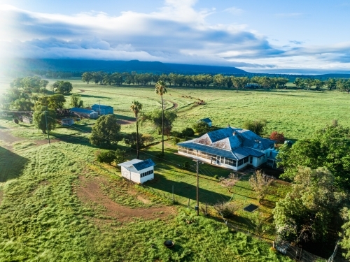 Morning sunlight bursting over small country farmstead and green paddocks - Australian Stock Image