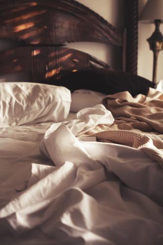 Morning sunlight on an unmade luxury bed of white sheets and beige blanket - Australian Stock Image
